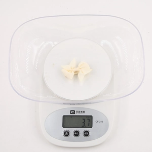 Macro shot of a cream grosgrain ribbon bow on a scale showing 3.7g weight