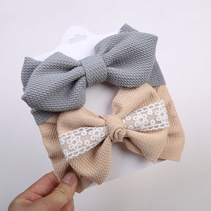 Détail de deux bandeaux bébé gaufrés en gris et beige avec nœuds en dentelle blanche