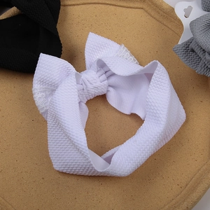 Détail d'un bandeau bébé en tissu gaufré blanc avec décoration de nœud en dentelle