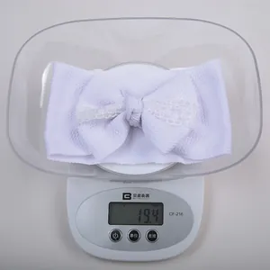 Gros plan d'un bandeau blanc léger en dentelle pour bébé pesé sur une balance numérique