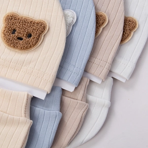 Close-up of ribbed cotton baby beanies with 3D plush bear patches in multiple colors