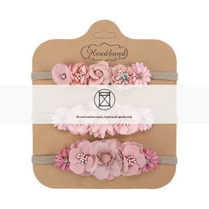 Three-piece baby headband set with pink floral designs and pearl accents on kraft card