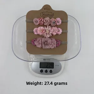Detailed view of three-piece baby floral headbands in pink and purple colors on a scale