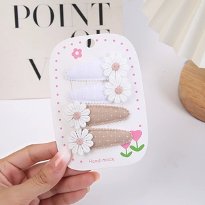 Détail de quatre barrettes en tissu faites main avec marguerites sur une carte