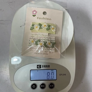 Détail de pinces à cheveux brodées de fleurs sur une balance pesant 8 grammes