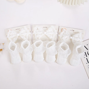Detailansicht von Baby-Stirnband und Socken-Set mit weißen Spitzenschleifen auf Karton