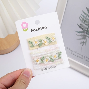 Détail de deux barrettes à fleurs brodées à la main avec dentelle sur carte de présentation