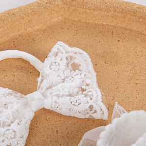 Detail von weißem besticktem Spitzen-Stirnband und passenden Babysocken auf Holz
