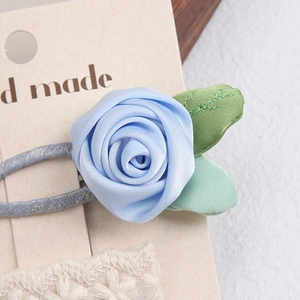 Detail of a handmade light blue satin rose hair clip with green leaves and lace accents