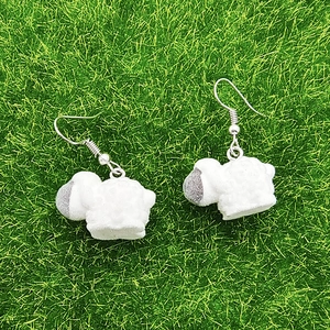 Close-up of cute cartoon sheep earrings with white flocked texture on green grass