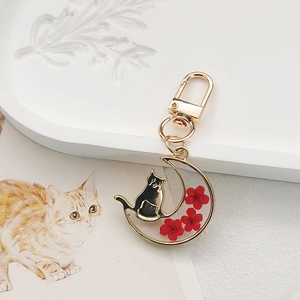 Detail of a golden crescent moon keychain with black cat silhouette and red flowers