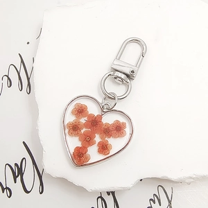 Macro shot of heart-shaped resin keychain featuring natural orange dried flowers and silver clasp