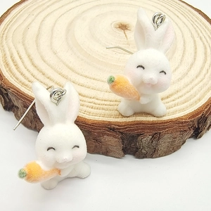 Detail of white flocked rabbit earrings with orange carrot on a rustic wood slice