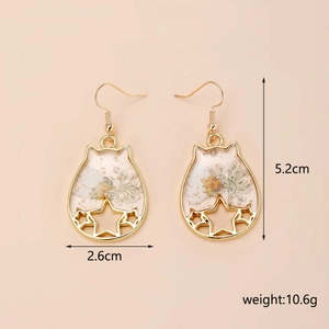 Détail des boucles d'oreilles chat avec fleurs séchées blanches et feuilles d'or en résine