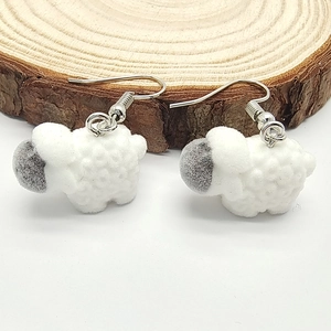 Macro detail of cute white flocked sheep earrings on a rustic natural wood surface