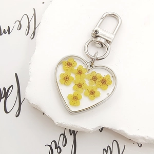Detail of heart resin keychain with yellow dried flowers on white textured stone
