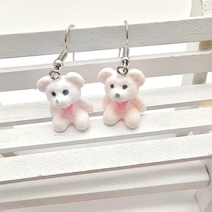 Detail view of cute pink flocked bear earrings with bows on a miniature white bench