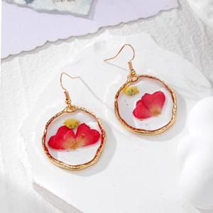 Detailed macro view of resin earrings with real red and yellow dried flowers and gold foil