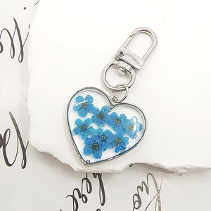 Macro view of a heart-shaped keychain with real blue dried flowers in transparent resin