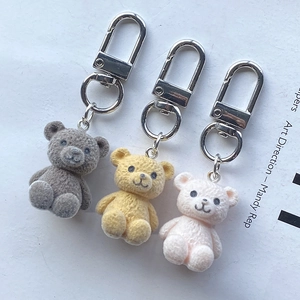Trois porte-clés ours floqués en gris, jaune et rose avec des fermoirs mousquetons en métal