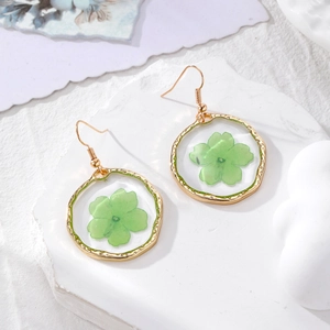 Detailed close-up of golden round earrings with real green dried flowers in clear resin