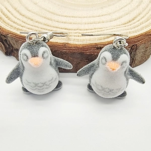 Cute flocked penguin drop earrings with classic grey and white finish on a wooden stand