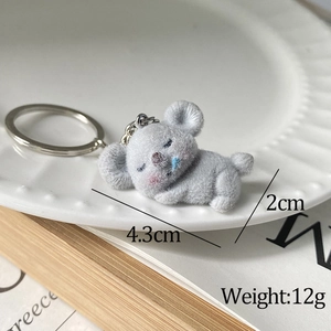 Close-up of cute grey flocked koala keychain sleeping on a white ceramic plate