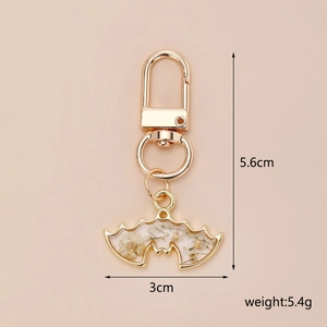Golden bat keychain with white dried flowers and resin, showing 5.6cm height dimensions