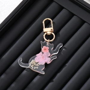 Cat-shaped resin keychain with dried flowers and gold metal clasp on a black tray