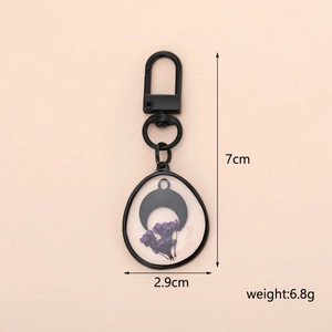 Detail view of black cat keychain with dried flowers showing 7cm height and 2.9cm width