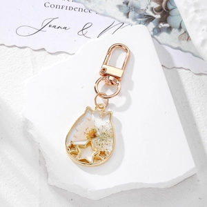 Detailed macro of cat-shaped gold metal pendant with dried flowers and gold foil inside