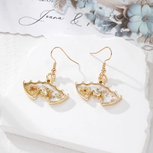 Boucles d'oreilles chauve-souris dorées avec résine et fleurs séchées sur marbre