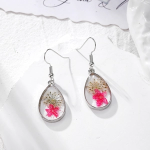 Close-up of teardrop resin earrings featuring natural pink and white dried flowers