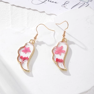 Dettaglio di orecchini a forma di ala con fiori secchi rosa in cornice dorata di resina