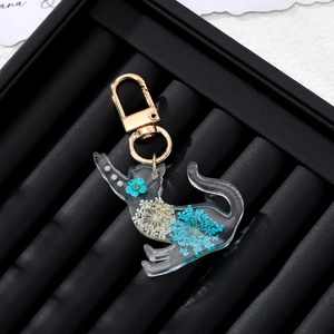 Close-up of resin cat keychain with blue dried flowers and golden metal hook