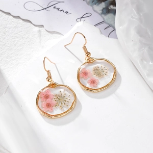 Détail de boucles d'oreilles en résine avec de vraies fleurs séchées et cadres dorés
