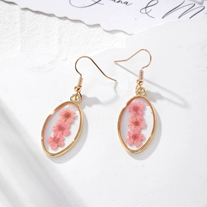 Dettaglio di orecchini ovali con fiori secchi rosa e cornice in metallo dorato