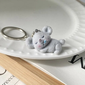 Cute flocked koala keychain in sleeping pose displayed on a ceramic plate for bag decoration