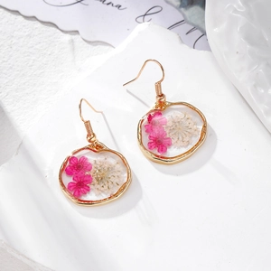 Détail de boucles d'oreilles en résine faites à la main avec de vraies fleurs séchées roses