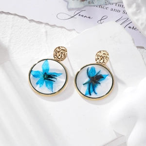 Detailed macro view of golden resin earrings with blue dried flowers on stone pedestal
