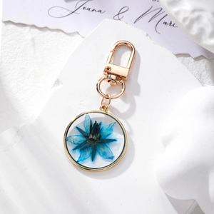 Detail shot of a golden metal keychain with blue dried flowers on a white stone tray