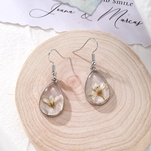 Macro detail of drop-shaped resin earrings with white dried flowers on wooden tray