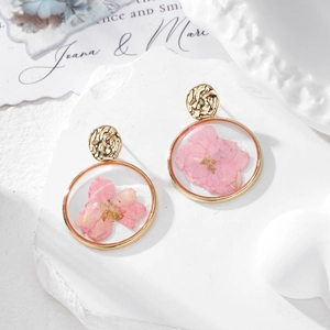 Elegant pink dried flower earrings in round golden metal frames on a stone display