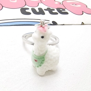 Close-up of cute white flocked alpaca pendant featuring a green heart-shaped bib
