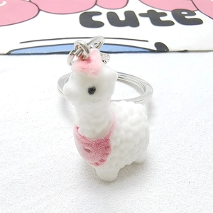Macro detail of a cute white flocked alpaca keychain with pink bib and hat decoration