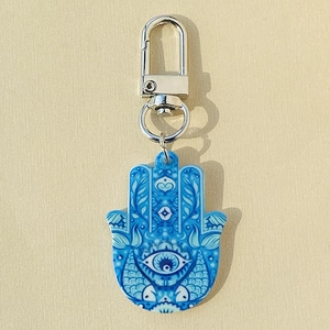 Detail of Hamsa hand keychain with evil eye pattern and blue tribal motifs on beige background