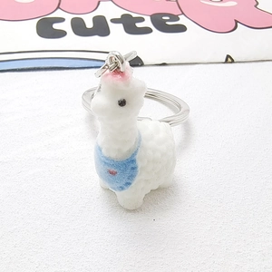 Close-up of white flocked alpaca keychain with blue bib and pink flower detail