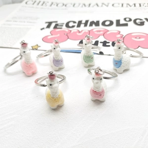 Set of 6 cute flocked alpaca figurines as colorful keychain charms on textured white surface