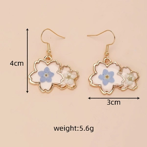 Detail view of 4cm gold-framed earrings with white and blue dried flowers in resin