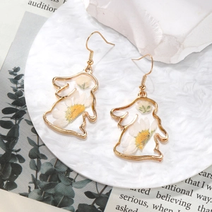 Macro shot of gold rabbit earrings featuring real white dried flowers in resin